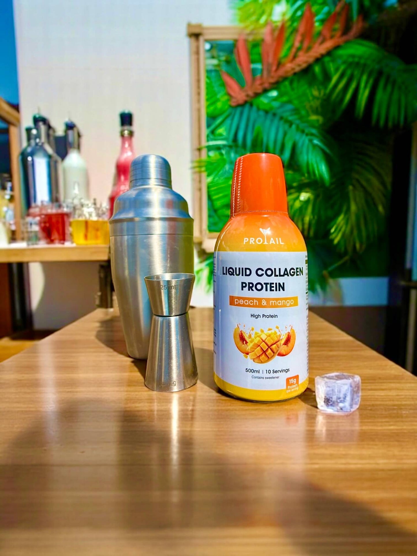 Protein supplement bottle on a table with cocktail shaker and glasses in the background